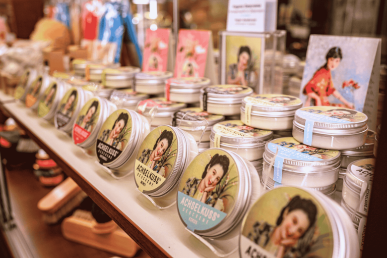 Regal im Geschäft von Walter Weiss in Wien mit mehreren Dosen ACHSELKUSS Deocreme, aufgereiht in verschieden Sorten